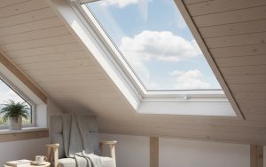 Fenêtre de toit VELUX avec clapet de ventilation ouvert dans un intérieur de combles lumineux.